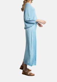 Pull en tricot bleu clair à manches trois-quarts, associé à une jupe plissée et fluide bleu clair, et des sandales marron à deux boucles.