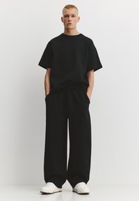 Maglietta oversize in cotone nero e pantaloni abbinati ampi con vita elastica; abbinati a sneakers bianche e un design minimalista.