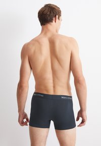 Černé boxerky s přiléhavým střihem a páskem s logem, zobrazené ze zadní strany, ukazující hladkou, elastickou látku a minimalistický styl.