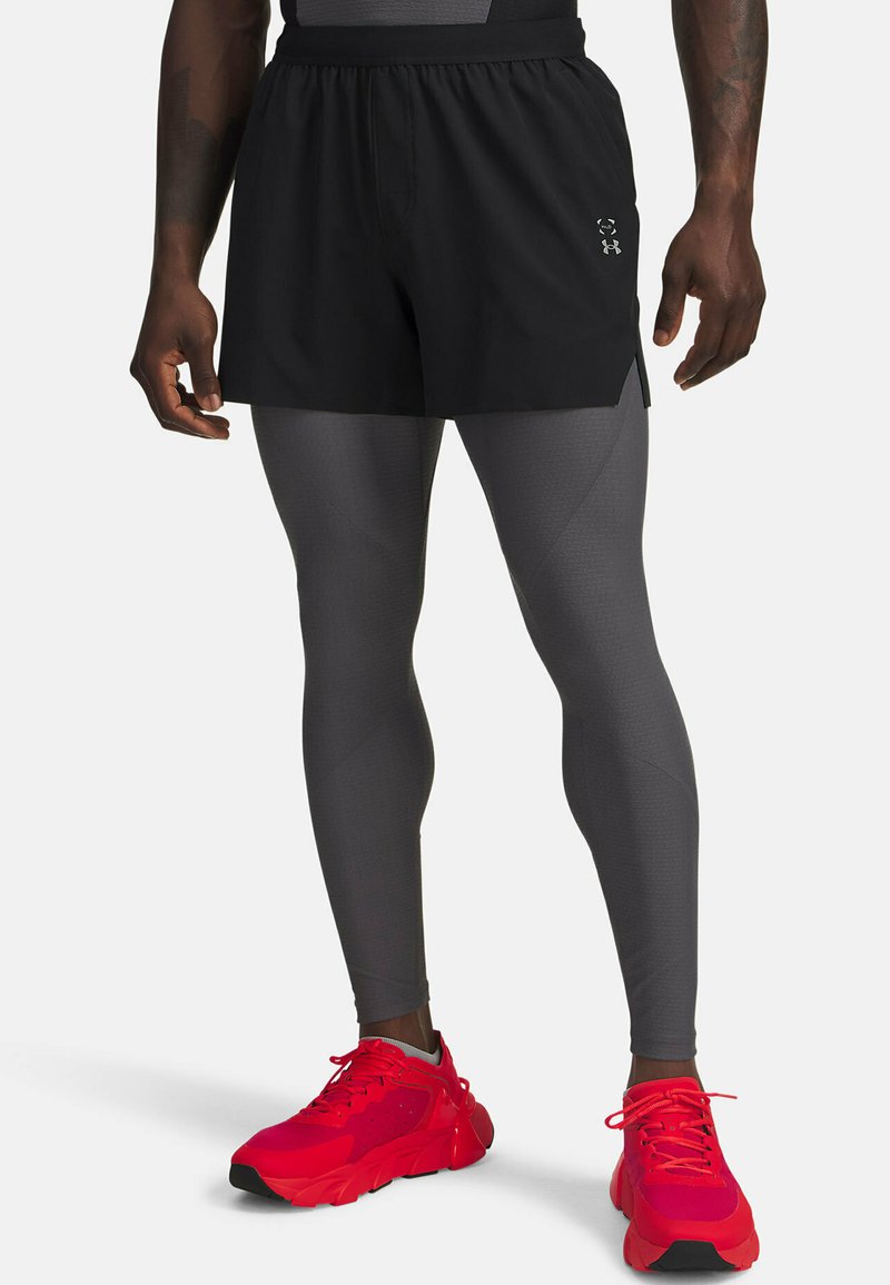 Shorts deportivos negros sobre leggings grises, complementados con zapatillas rojas. Los shorts cuentan con un material ligero y sutiles aberturas laterales.