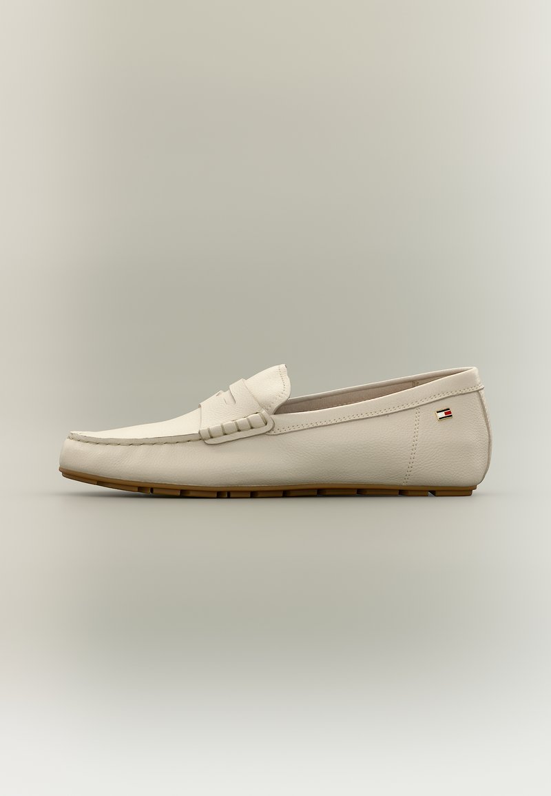 Mocassin en cuir beige avec semelle en caoutchouc marron, détails cousus et petit logo rectangulaire sur le côté du talon, sur un fond neutre.