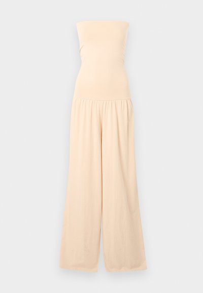 Μπεζ ολόσωμη φόρμα χωρίς τιράντες με εφαρμοστό μπούστο και παντελόνι με φαρδιά πόδια, συγκεντρωμένη στη μέση, παρουσιάζεται πάνω σε ανοιχτό γκρι φόντο.