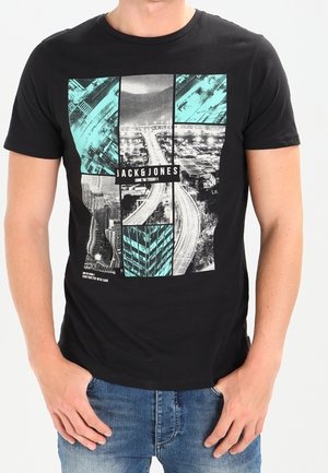 Homme portant un t-shirt noir Jack & Jones avec un motif de paysage urbain bleu et gris divisé en panneaux rectangulaires, associé à un jean bleu.