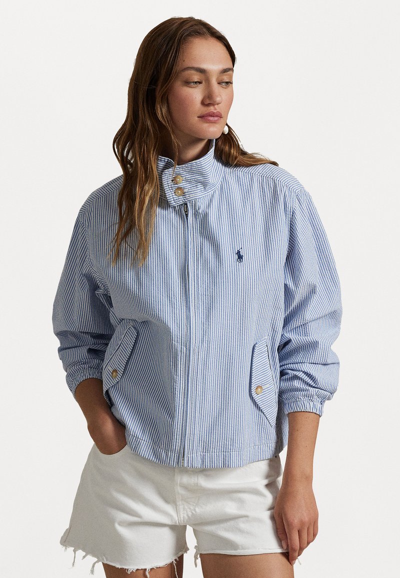 Casaco listrado em azul e branco com gola alta, fecho de correr na frente e bolsos laterais, apresentando botões dourados e punhos canelados.