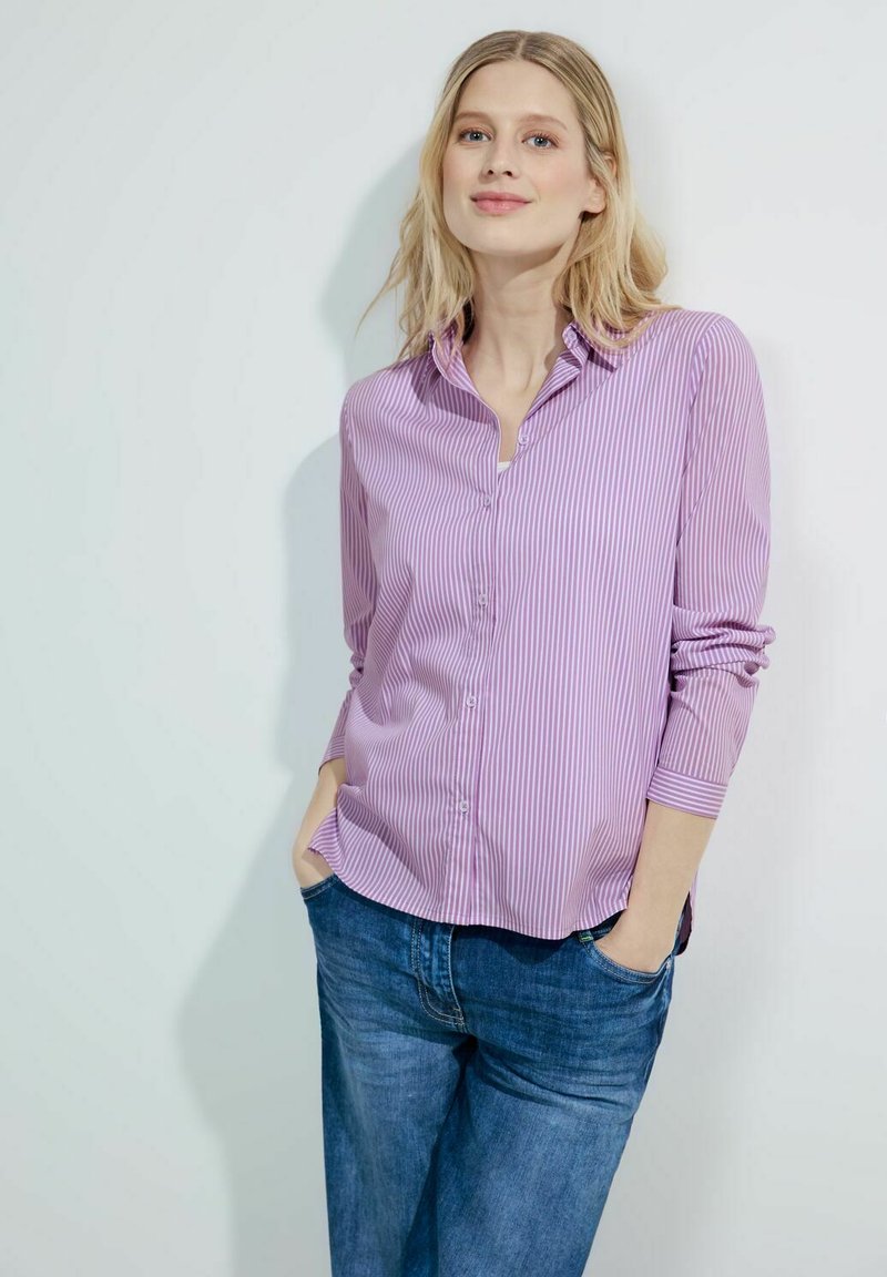 Striped button-up shirt in light purple and white, featuring a collar, long sleeves, and a relaxed fit. Worn with blue denim jeans.