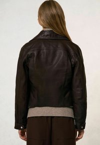 Jachetă din piele de culoare maro închis, cu un design ajustat, care include un guler, detaliu cu fermoar și un pulover texturat la baza. Finisajul texturat este vizibil.