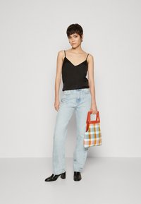Black satin camisole with thin straps, light blue straight-leg jeans, and a checked handbag in orange, blue, and yellow. Black block-heeled boots.