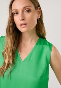 Green sleeveless top with a V-neck design, made of smooth fabric. Features a simple cut and minimalistic style, no patterns or accents.