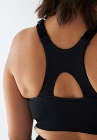 Czarny sportowy stanik z przodem typu racerback, wykonany z teksturowanej tkaniny, z małym tłoczonym logo serca na środku pleców.
