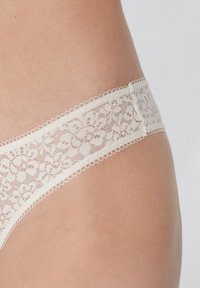 Culotte en dentelle couleur crème, ornée d'un motif floral et de bords délicatement festonnés, avec une texture douce et une taille lisse.