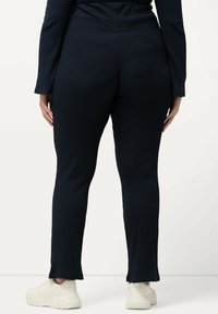Mörkblå ribbade leggings med en figurnära design, som har midjeband i bred modell och diskreta sidoflikar vid anklarna, ihop med ljusa sneakers.