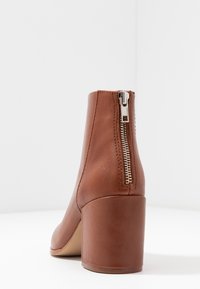 Botte chelsea en cuir marron avec un talon empilé, dotée d'un détail de fermeture éclair argentée à l'arrière et d'une texture lisse.
