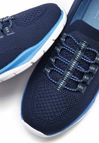 Scarpe da ginnastica a rete blu navy con accenti blu, tomaia testurizzata e un sistema di allacciatura elastico unico. Suola in gomma bianca con dettagli ammortizzati.