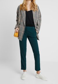 Rutigt svart och vitt oversize blazer, svart topp, teal byxor och vita sneakers. Liten gul handväska som accent.