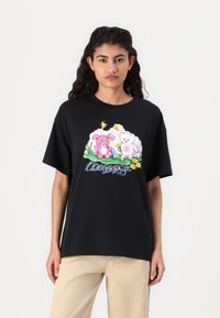 Schwarzes Baumwoll-T-Shirt mit einem verspielten Grafikdesign eines rosa Schweins und eines weißen Kaninchens mit Blumen, vor einem bunten Hintergrund.