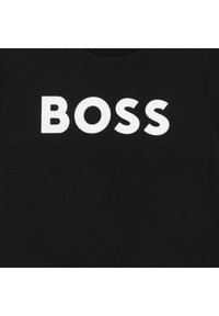 Juoda medvilninė marškinėliai su didelėmis baltomis blokinėmis raidėmis, sudarančiomis žodį „BOSS“. Apvalios kaklo dizainas su lygiu paviršiumi.