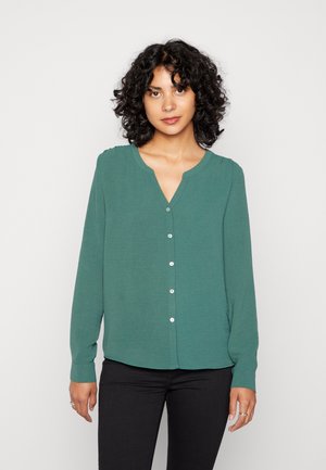 Blusa verde de manga longa com decote em V e fechamento por botões, apresentando um tecido suave e detalhes levemente franzidos nos ombros.