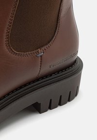 Gros plan d'une botte en cuir marron avec un panneau latéral élastique et une épaisse semelle noire rainurée.