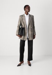 Grau kariertes, doppelt geknöpftes Blazer, weißes Hemd, schwarze weit geschnittene Hose, schwarze Handtasche und schwarze spitz zulaufende Absätze. Minimalistische Designelemente.