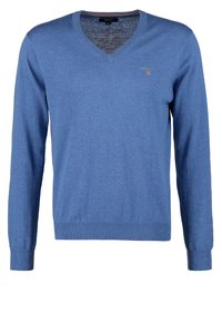 Pull bleu homme à col en V et manches longues, avec bord-côtes aux poignets et à l’ourlet, avec un petit logo sur le côté gauche de la poitrine.