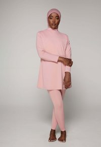 Roze tuniekjurk met een hoge hals en lange mouwen, gecombineerd met bijpassende legging; gladde stof, minimaal ontwerp en getailleerd silhouet.