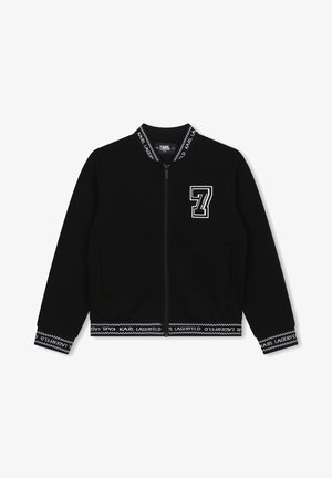 Chaqueta negra con cremallera y parche blanco con el "7" en el lado izquierdo del pecho, con cuello, puños y dobladillo acanalados de la marca que dicen "Karl Lagerfeld."