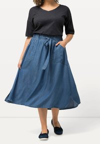 Denim midi kjol med elastiskt midjeband och knytt detalj. Två sidofickor, sidoklyftor och en flödande silhuett i en medelblå nyans.