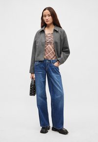 Γκρι cropped μπουφάν πάνω από ένα τοπ με σχέδια, συνδυασμένο με φαρδιά μπλε τζιν και μαύρα chunky παπούτσια, κρατώντας μια μαύρη τσάντα με τρουκς.