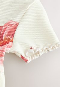 Material alb cu dungi, având un design floral roz și o margine cu volane la mânecă. Texturat cu linii verticale subtile.