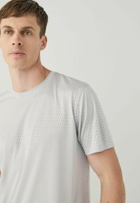 Light gray short-sleeve shirt with a textured pattern of small squares and dots. Round neckline, smooth fabric, and a regular fit.