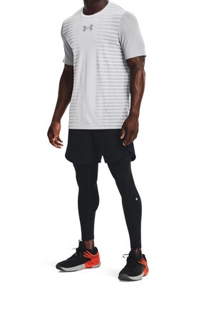 Mann trägt weißes kurzärmliges Sportshirt, schwarze Laufshorts über schwarzen Leggings und schwarze sowie orangefarbene Laufschuhe.