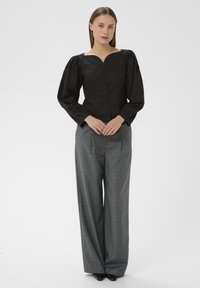 Bluză neagră ajustată cu mâneci bufante și decolteu în V, având o serie de nasturi pe față. Asortată cu pantaloni largi din țesătură în carouri gri.