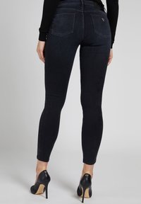 Jeans skinny neri con una trama liscia, dotati di due tasche posteriori e un piccolo dettaglio del logo. Abbinati a scarpe con tacco alto nere.