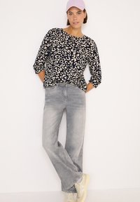 Blusa a stampa leopardata in blu navy e beige, maniche a tre quarti, abbinata a jeans a gamba larga grigio chiaro e sneakers beige. Cappellino lavanda incluso.