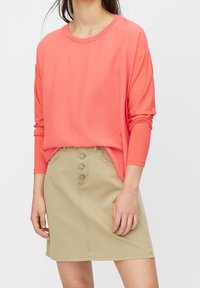 Korálový dlouhý rukáv top spárovaný s béžovou sukní ke kolenům s designem na knoflíky vepředu a bočními kapsami. Hladká textura celkově.