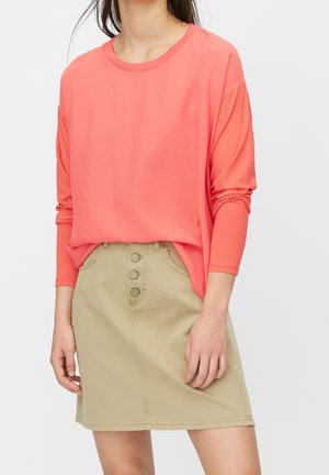 Haut à manches longues corail associé à une jupe beige à mi-longueur avec un design à boutons sur le devant et des poches latérales. Texture lisse dans l'ensemble.