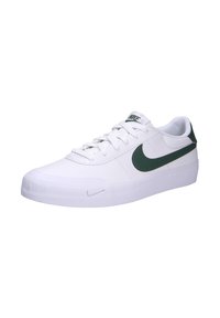 Zapatilla blanca con acentos verdes, con una parte superior de sintético suave, cordones planos, punta redondeada y suela de goma texturizada. Branding de Nike visible.