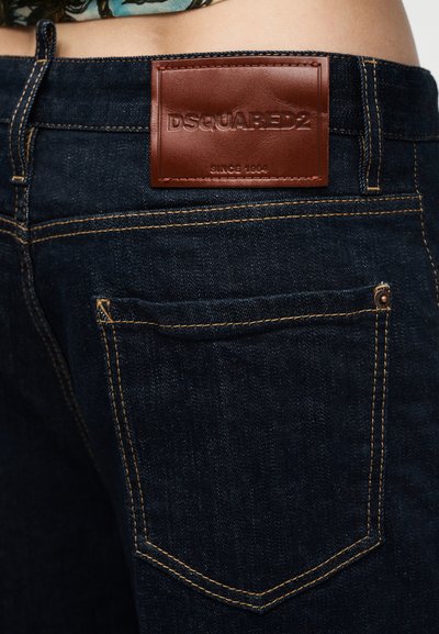Σκούρο μπλε τζιν μεραμμένες πίσω τσέπες και καφέ δερμάτινο ταμπελάκι με την επιγραφή "DSQUARED2 Since 1964" στη μέση.