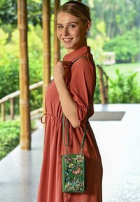 Groene leren schoudertas met bloemen- en vlinderborduursel, met een slank ontwerp en een verstelbare strap, gedragen met een koraalkleurige jurk.