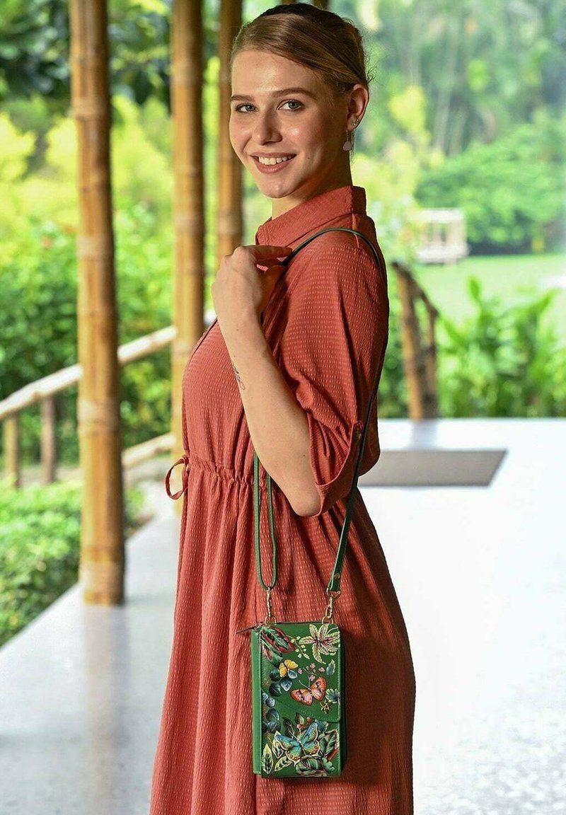 Groene leren schoudertas met bloemen- en vlinderborduursel, met een slank ontwerp en een verstelbare strap, gedragen met een koraalkleurige jurk.