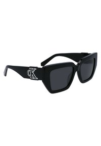 Ochelari de soare negri cu lentile pătrate, design îndrăzneț și rame groase. Prezintă un logo alb 'CK' pe braț pentru branding.