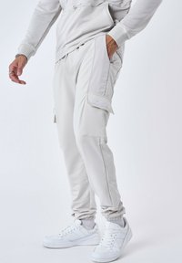 Lichtgrijze cargobroek met ritszakken, tapered fit en elastische boorden. Gecombineerd met witte sneakers en een gestructureerde stof.
