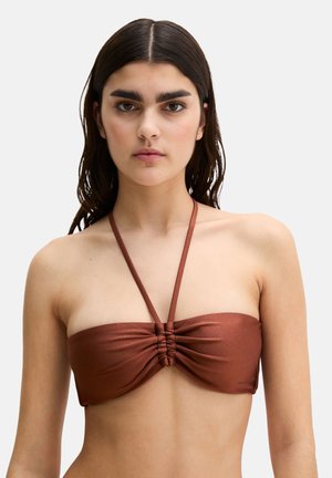 Young woman with long dark hair wearing a rust-colored bandeau bikini top with a thin halter neck strap.