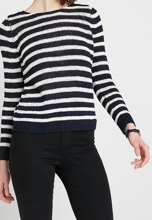 Stripet sweater i marineblå og hvid, strikket tekstur, lange ærmer, ribbede manchetter og kant, parret med sorte bukser.