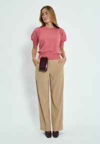Maglione rosa a maniche corte lavorato a maglia con bordi a coste abbinato a pantaloni beige a gamba larga. Borsa a tracolla marrone attaccata alla vita.