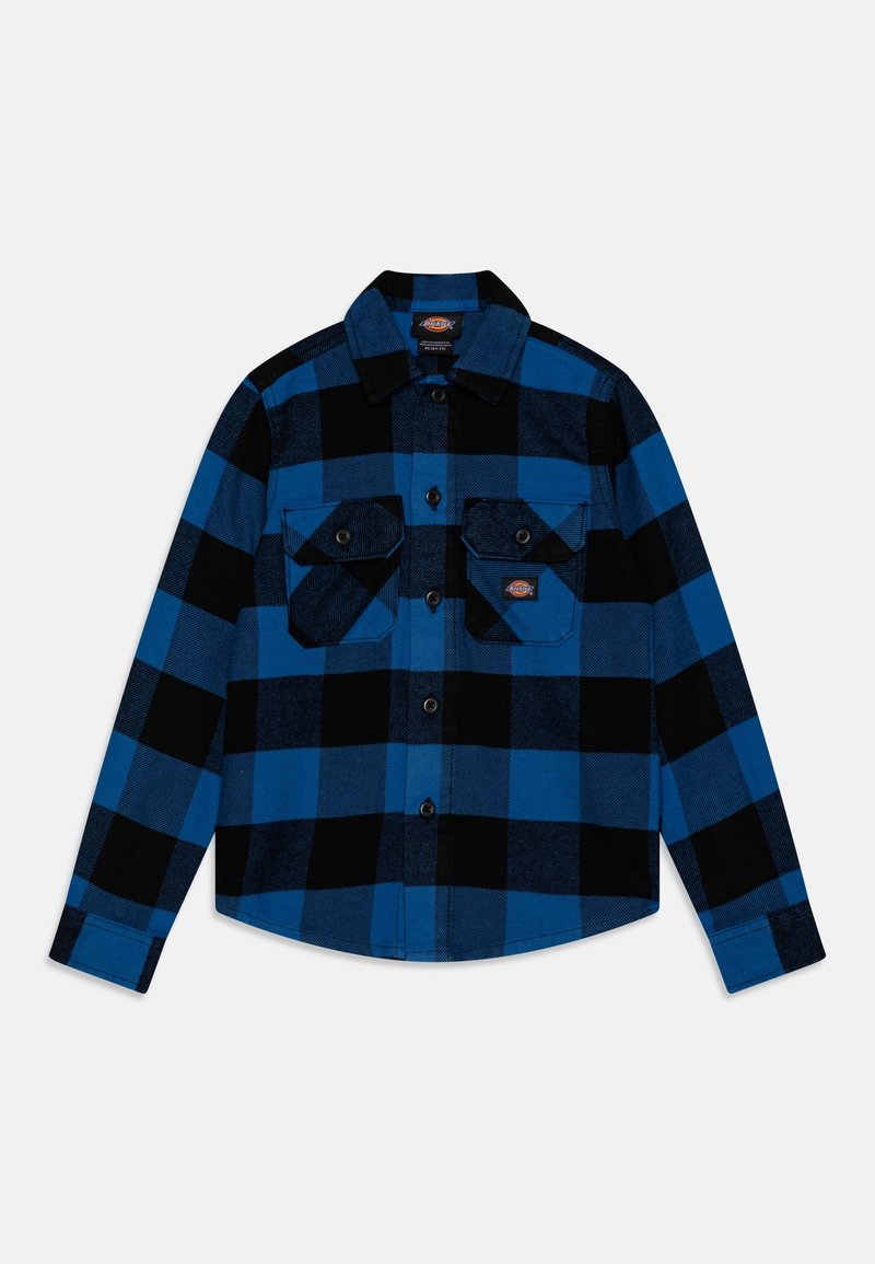 Chemise à carreaux bleue et noire à manches longues, boutonnée, avec deux poches poitrine boutonnées sur fond blanc.