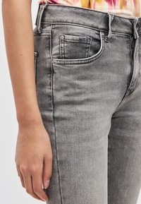 Szare dżinsy z denimu o dopasowanym kroju, średnim stanie, tradycyjnym fasonie z pięcioma kieszeniami oraz subtelnymi przetarciami.