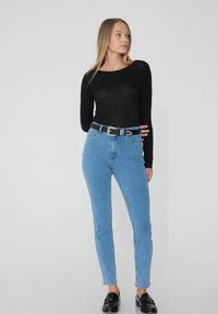 Světle modré džíny s vysokým pasem a přiléhavým střihem, spárované s černým topem s dlouhým rukávem a dekorativním černým opaskem. Nosit černé mokasíny.