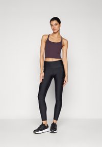 Sorte atletiske leggings med høj talje suppleret med en mørk lilla forkortet tanktop. Modellen har sorte løbesko på.