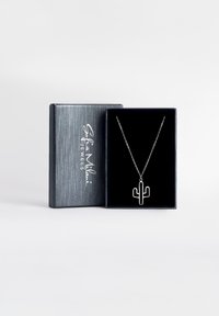 Collana con pendente a forma di cactus in argento esposta in una scatola foderata in velluto nero con un esterno scuro e testurizzato. Catena visibile, design delicato.